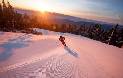 Skier carves on groomed trail at sunrise in Stowe, VT.