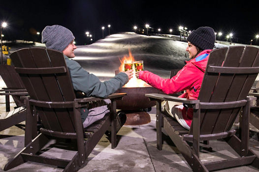 A couple relax around firepit at the base of Wilmot Mountain
