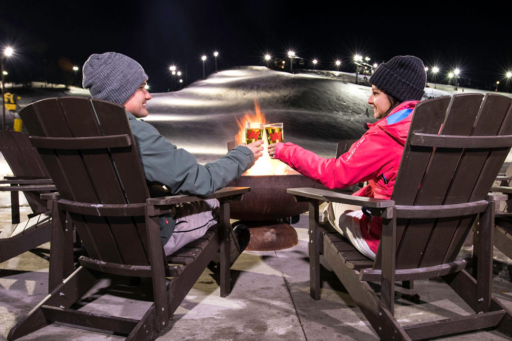 A couple relax around firepit at the base of Wilmot Mountain