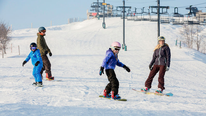 Family snowboards together on a groomed trail in Mt. Brighton, MI.