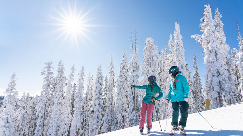 Two women ski North Peak on a blue sky day with fresh snow in Keystone, CO