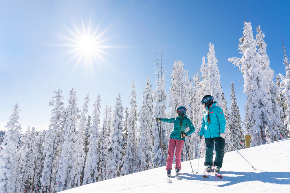 Two women ski North Peak on a blue sky day with fresh snow in Keystone, CO