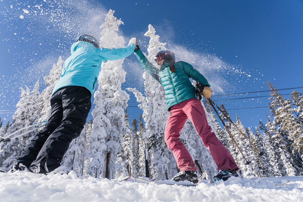 Two women ski North Peak on a blue sky day with fresh snow in Keystone, CO