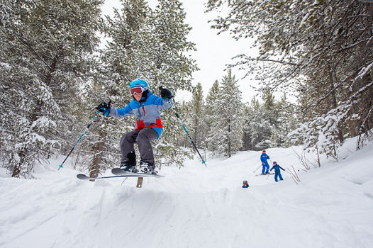 Kids ski group airing a jump in the woods at Crested Butte