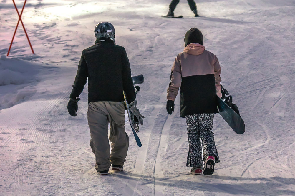 Two Snowboarders Walk Toward Terrain Park at Twilight at Alpine Valley
