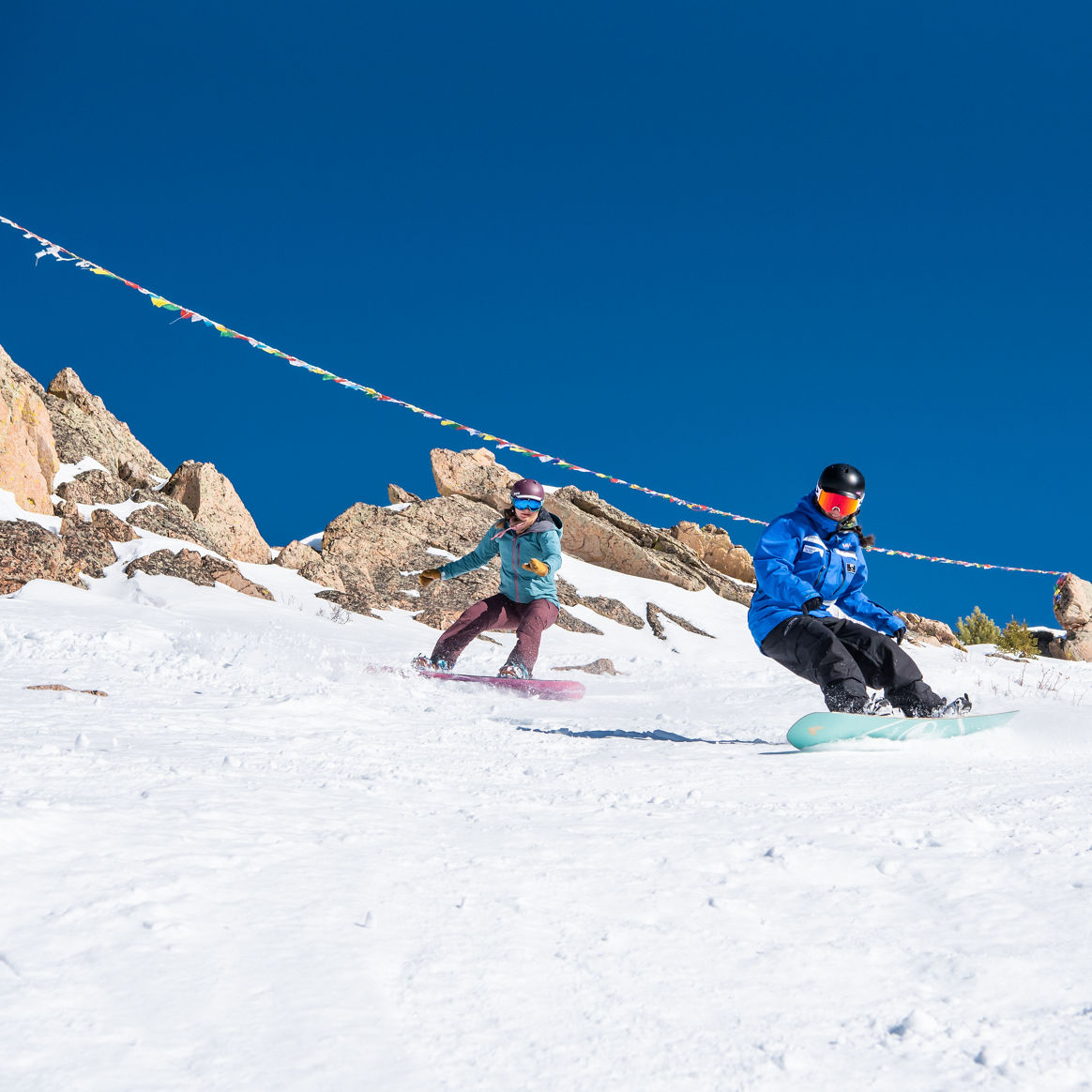Adult snowboard instructor rides in front of prayer flags at Crested Butte