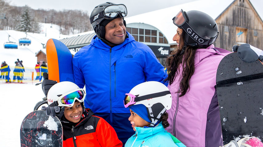 Family with Snowboards Smiling in Front of Bluebird Express