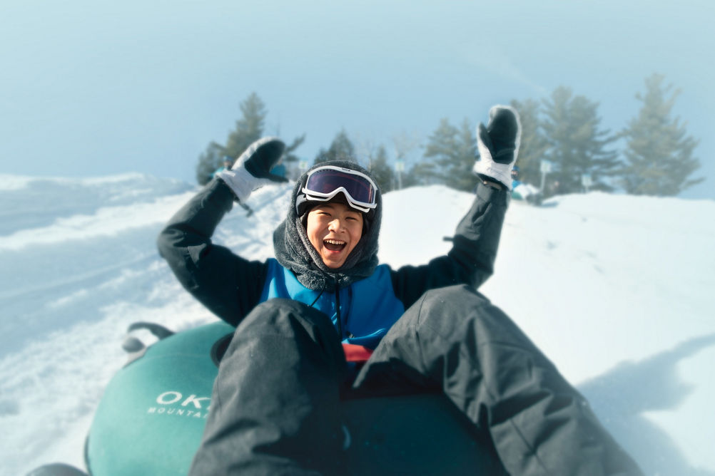 Child Tubing with Arms Up and Smiling in Okemo