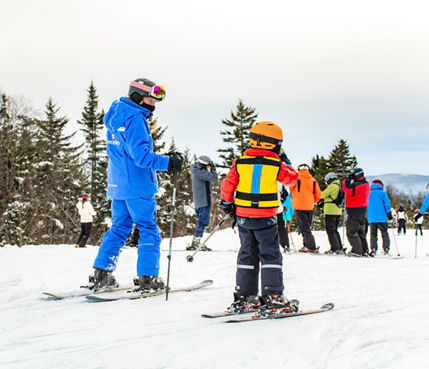 An instructor teaches a child how to ski at Okemo
