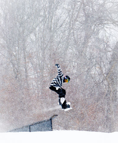 Snowboarder launches from a terrain park feature on a snowy day at Snow Creek