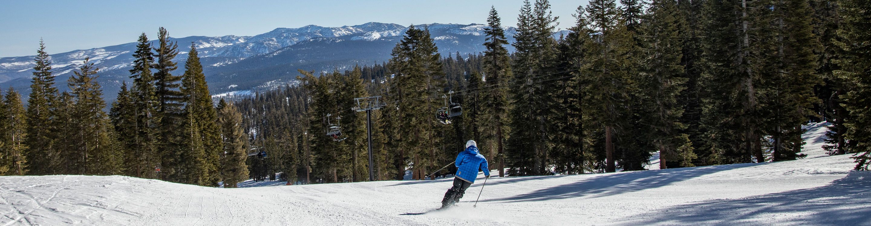 Skier Takes Turns on Fresh Corduroy with Mountains in Background at Northstar