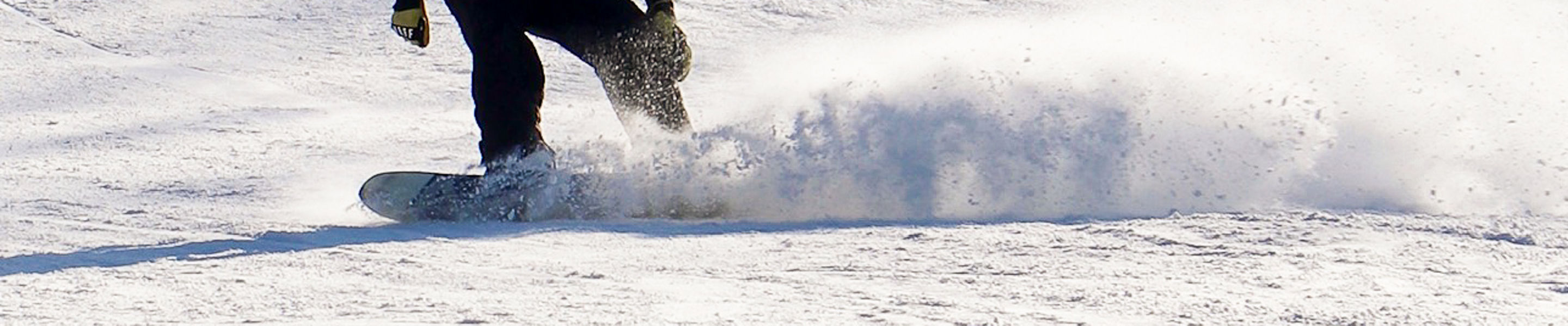 Snowboarder kicks up powder while guests ride a chairlift above at Snow Creek