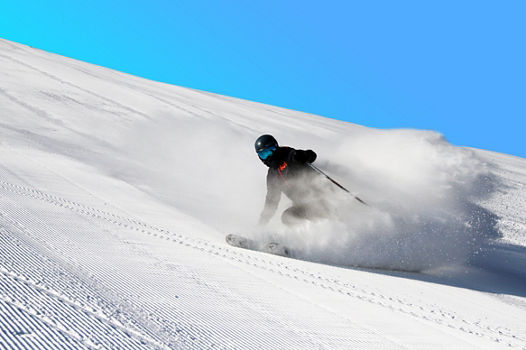A skier makes a powder cloud under blue sky at Mt Brighton