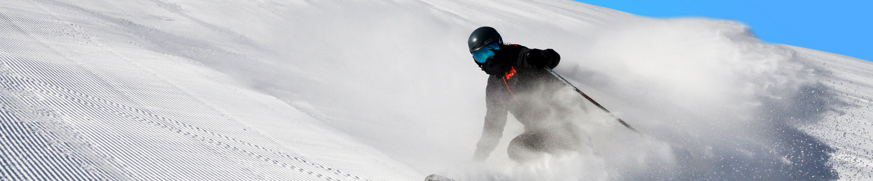A skier makes a powder cloud under blue sky at Mt Brighton