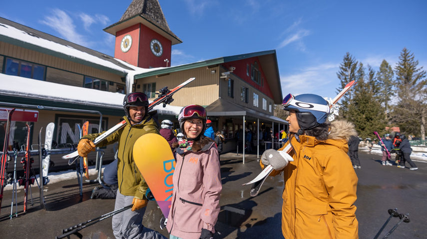 Friends Carrying Equipment Walk on Main Street in front of Clocktower at Mount Snow
