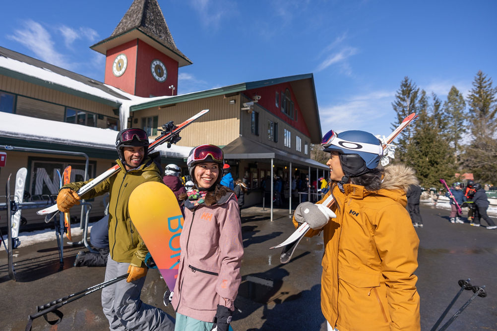 Friends Carrying Equipment Walk on Main Street in front of Clocktower at Mount Snow