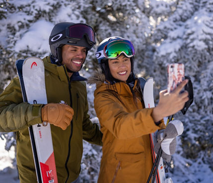 Couple Holding Skis Take Selfie in front of Snowy Trees at Mount Snow Summit