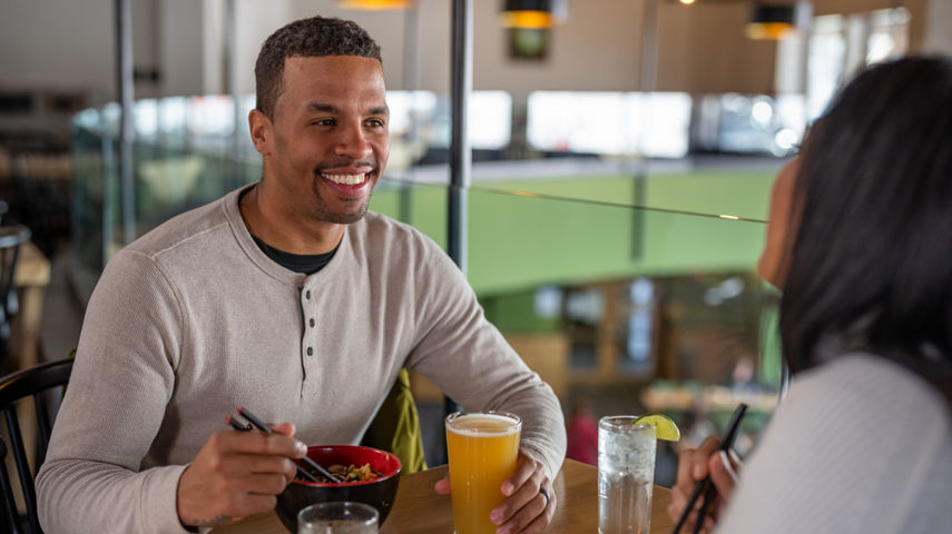 Couple Smiles Over Ramen Bowls and Drinks from High Timber in Carinthia Base Lodge at Mount Snow