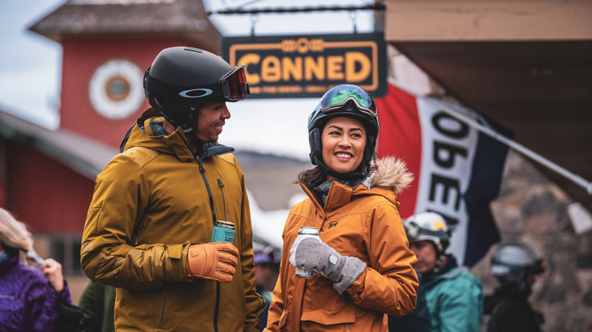 Couple Smiles with Beers in front of Canned Sign and Clocktower at Mount Snow