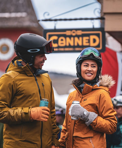 Couple Smiles with Beers in front of Canned Sign and Clocktower at Mount Snow