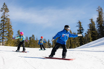 Young children snowboarding with an instructor