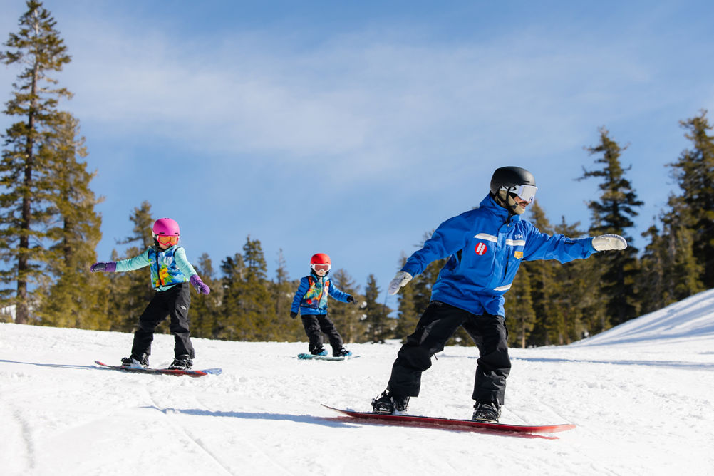 Young children snowboarding with an instructor