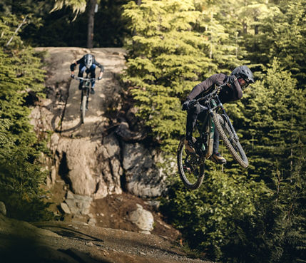 Two Mountain Bikers hitting features simultaneously 