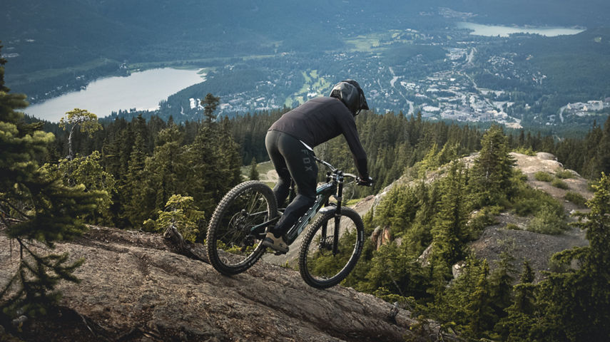 Mountain biker dropping rock with Whistler in background