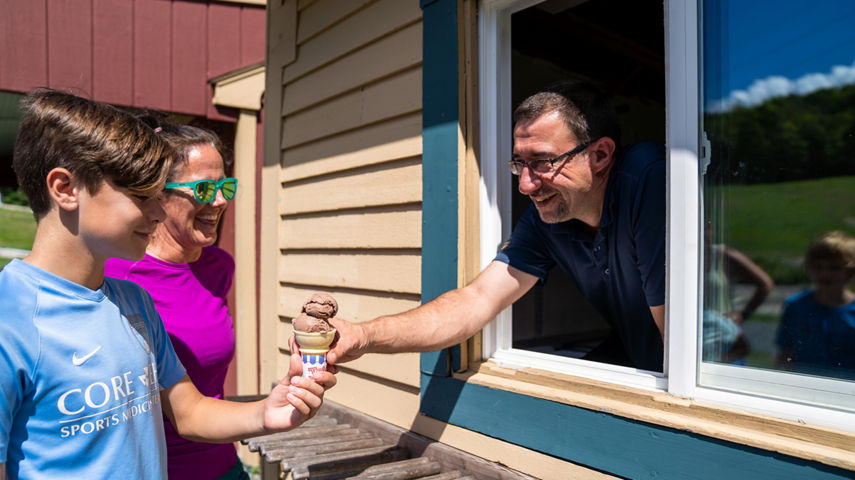 Man Hands a Young Boy a Chocolate Ice Cream Cone at Mount Sunapee