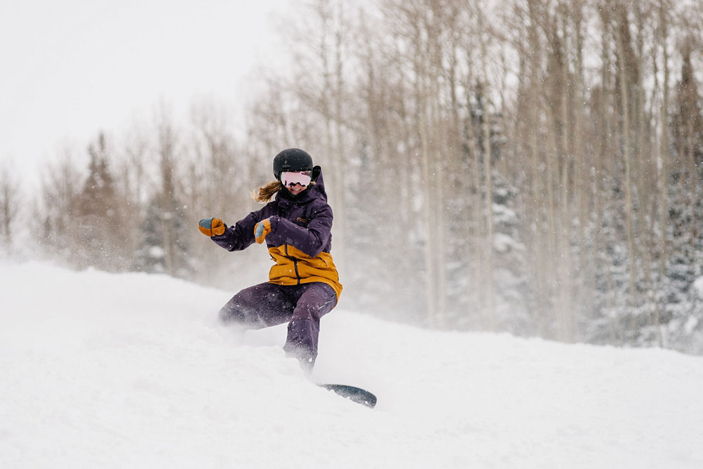 Snowboarder in Purple and Yellow Jacket Riding Down a Trail at Park City