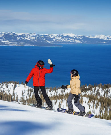 Snowboarders Prepare to High Five at the Top of a Run at Heavenly with a Scenic View of Lake Tahoe in the Background