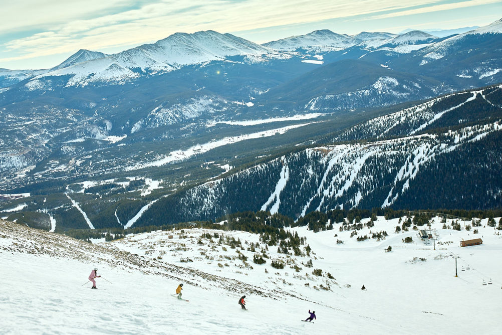 Skiers and Snowboarders Ride Down Trail with Scenic Background at Breckenridge