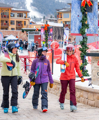 Three Friends Walk Through Canyons Village with Ski and Snowboard Gear at Park City