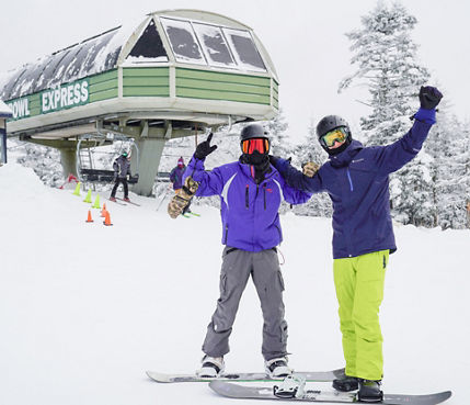 Guests Smile and Pose on Snowboards in Front of Chairlift at Mount Sunapee
