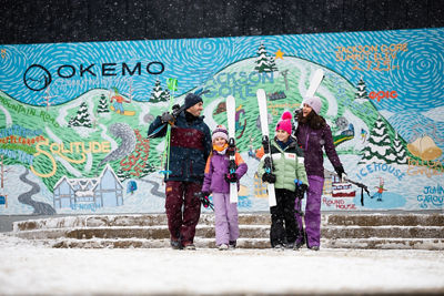 Family Carries Skis Heading Towards the Slopes in Front of Okemo Anniversary Sign