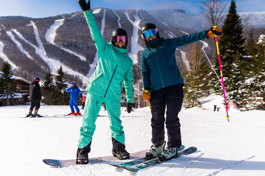 A Skier and a Snowboarder Smiling and Waving While Riding at Stowe