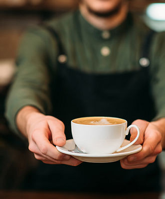 Waiter in black apron stretches a cup of coffee